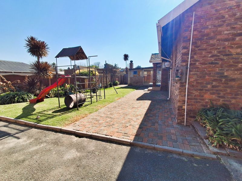 A rear exterior view of the property featuring a brick facade, paved walkway, and a well-maintained lawn area.