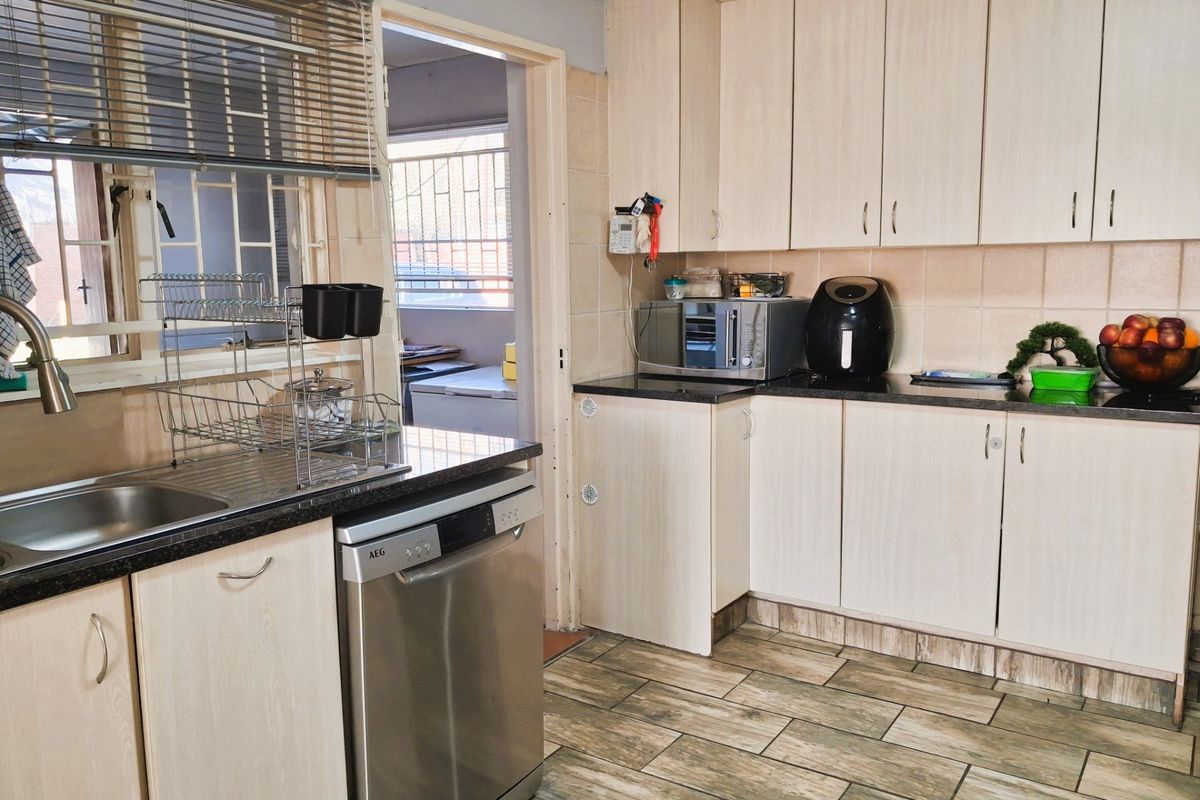 A functional kitchen featuring light-toned laminate cabinetry, dark granite countertops, tiled flooring, and a stainless steel dishwasher.