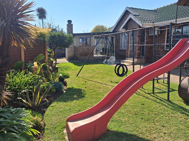 Rear garden view featuring a brick facade, paved patio area, and established lawn space.