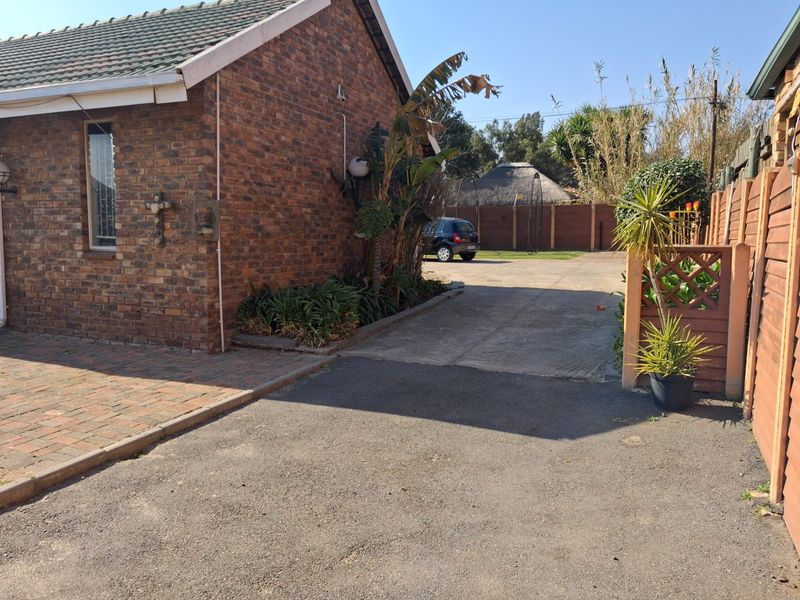 Exterior view of the property featuring a brick facade, tiled roof, and a combination of paved and asphalt driveway space.