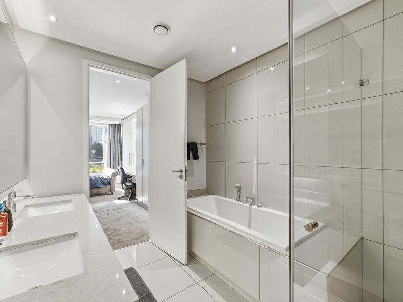 Modern bathroom featuring a double vanity, built-in bathtub, and a glass-enclosed shower area with neutral tiling and recessed lighting.