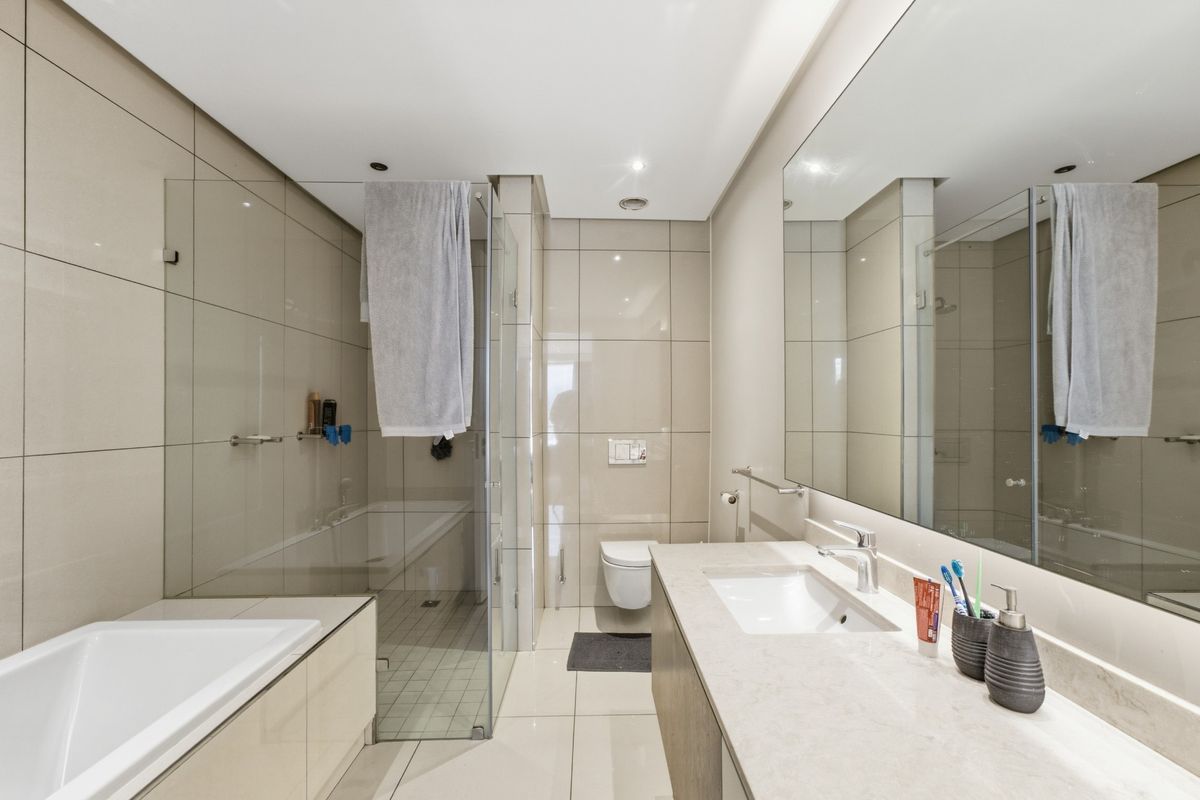 Modern bathroom featuring a wall-mounted toilet, glass-enclosed shower, built-in bathtub, and a sleek vanity with a large mirror.