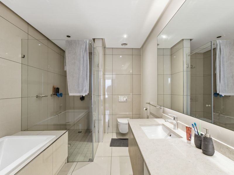Modern bathroom featuring a wall-mounted toilet, glass-enclosed shower, built-in bathtub, and a sleek vanity with a large mirror.