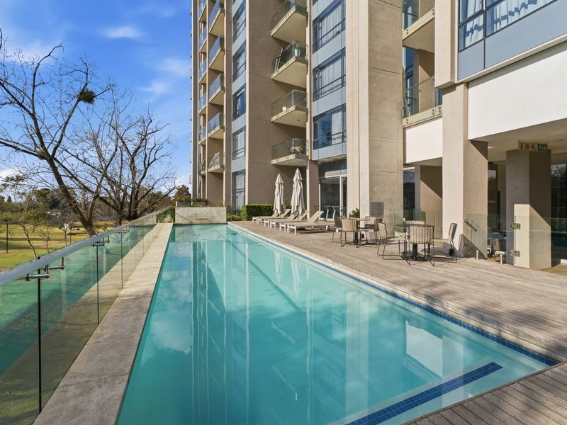 A well-maintained outdoor swimming pool area featuring timber decking, stone coping, and a modern glass balustrade overlooking the surrounding landscape.