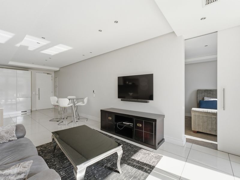Modern open-plan living area featuring sleek porcelain floor tiles, recessed lighting, and a seamless transition to the kitchen and adjacent bedroom space.