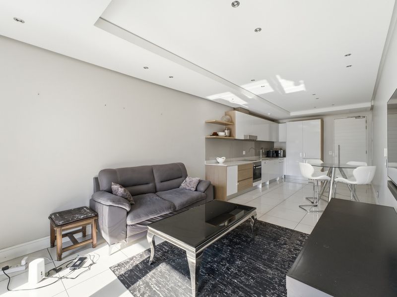 Modern open-plan living area featuring a sleek kitchen with built-in cabinetry, integrated appliances, and bright tiled flooring throughout the space.