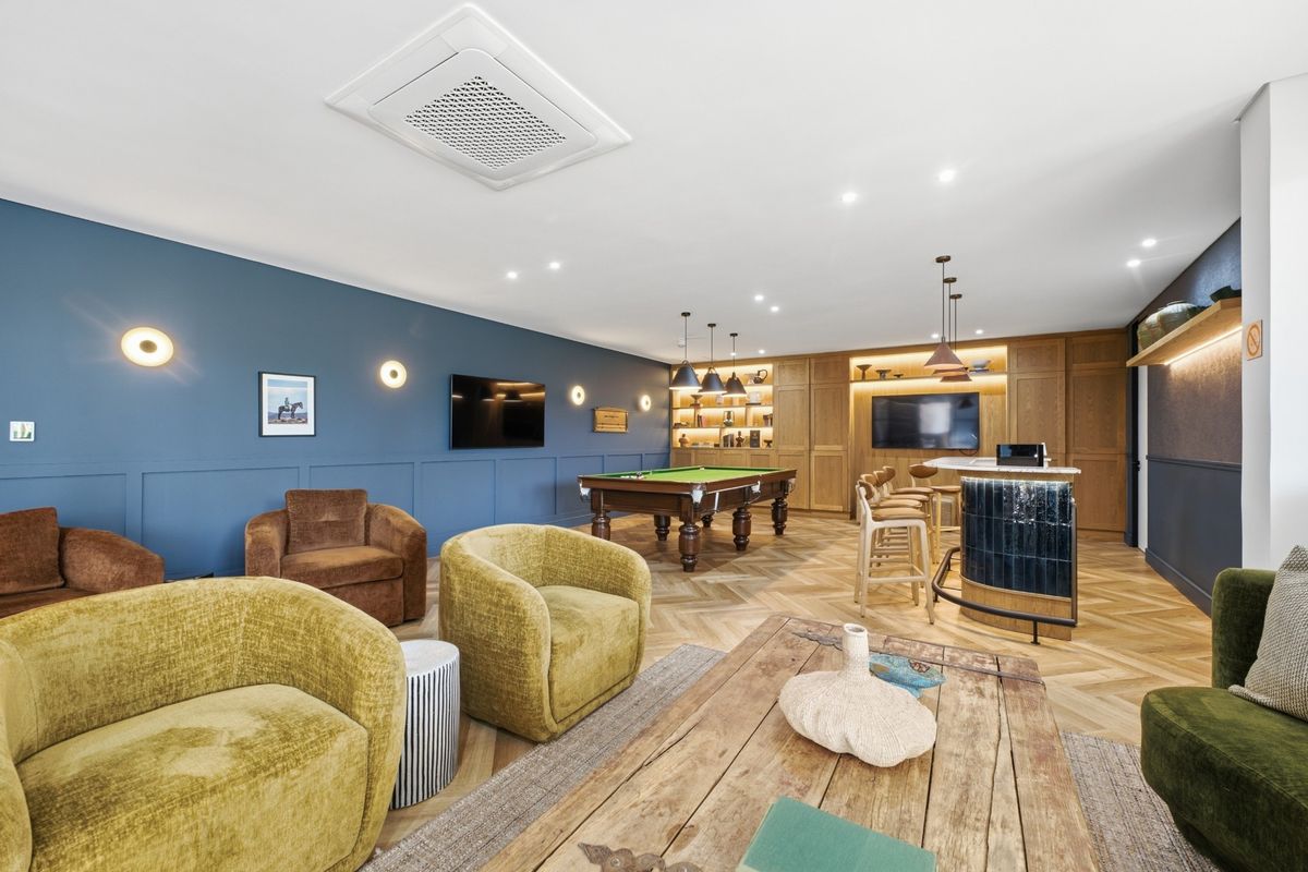 A sophisticated, well-appointed living and entertainment area featuring herringbone timber flooring, custom built-in cabinetry, a stylish bar, and integrated ceiling lighting.