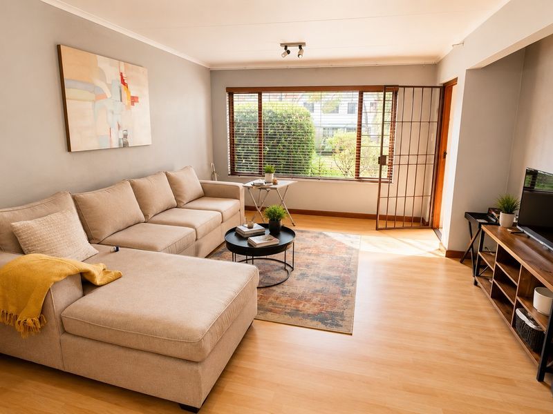 A bright and well-maintained living room featuring laminate flooring, neutral wall tones, and a security gate leading to the exterior.