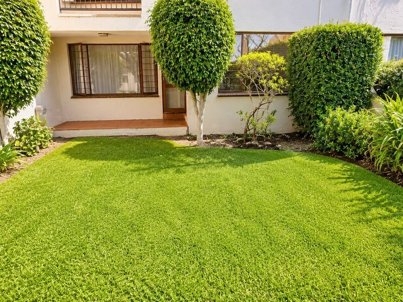 A well-maintained rear garden featuring a manicured lawn, established shrubs, and a small tiled patio area adjacent to the apartment building.
