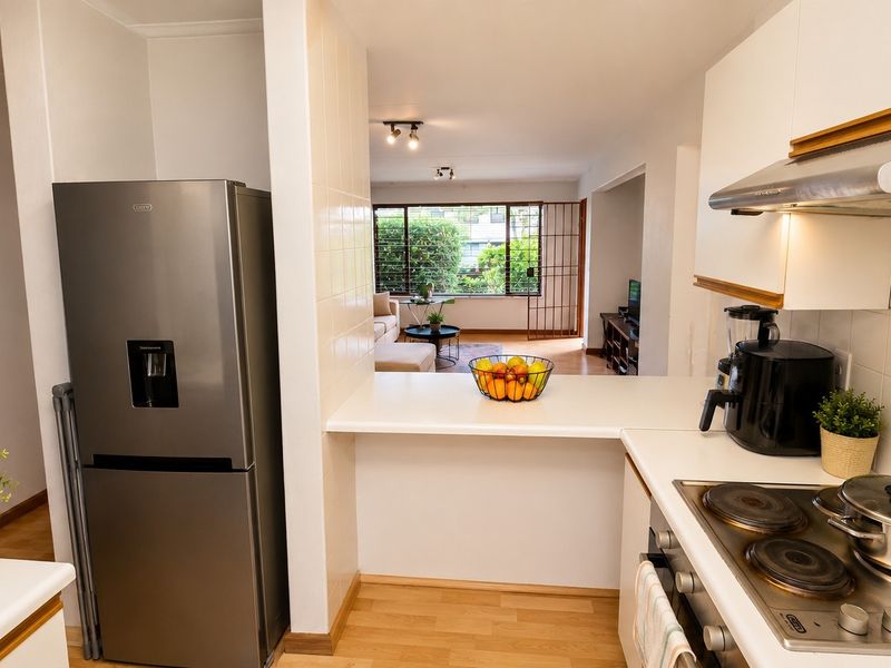 Open-plan kitchen featuring a breakfast bar, electric hob, and extractor fan, flowing seamlessly into the adjacent living area with large windows.