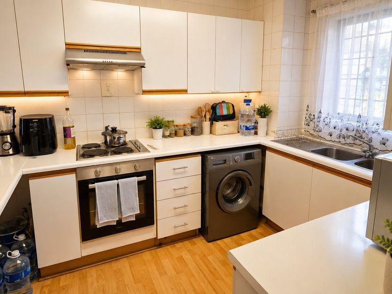A functional kitchen featuring white cabinetry, integrated oven and hob, tiled backsplash, and a double sink with natural light from the window.