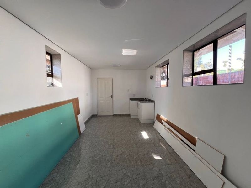 An empty, unfinished kitchen area featuring tiled flooring, built-in cabinetry with a sink, and multiple windows providing natural light.