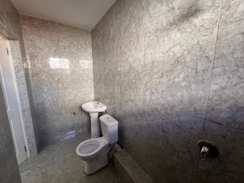 A clean, tiled bathroom featuring a pedestal washbasin, toilet, and shower plumbing, presenting a neutral and functional space ready for final touches.