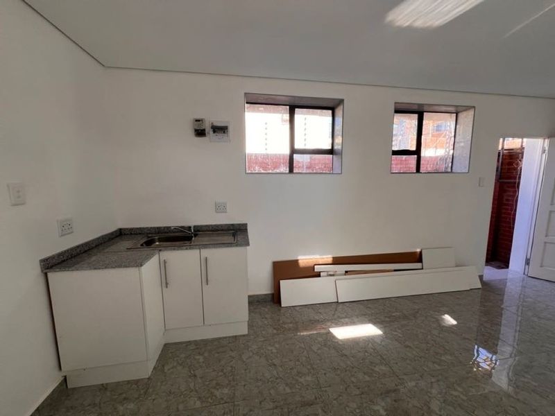 A compact, empty kitchen area featuring granite countertops, a stainless steel sink, built-in white cabinetry, and tiled flooring.