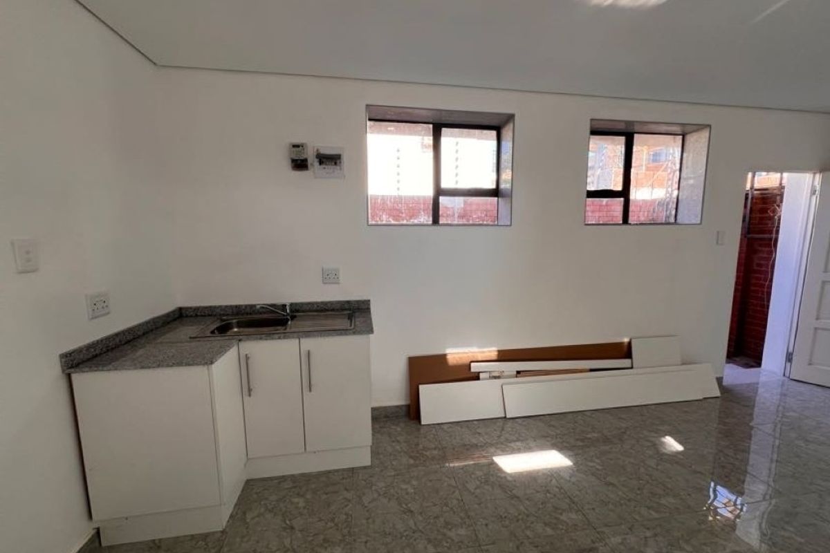 A compact, empty kitchen area featuring granite countertops, a stainless steel sink, built-in white cabinetry, and tiled flooring.