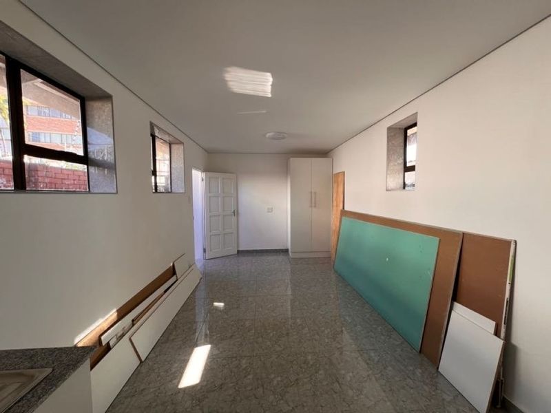 A spacious, empty bedroom featuring tiled flooring, built-in wardrobe, and natural light from multiple windows, currently undergoing minor finishing work.
