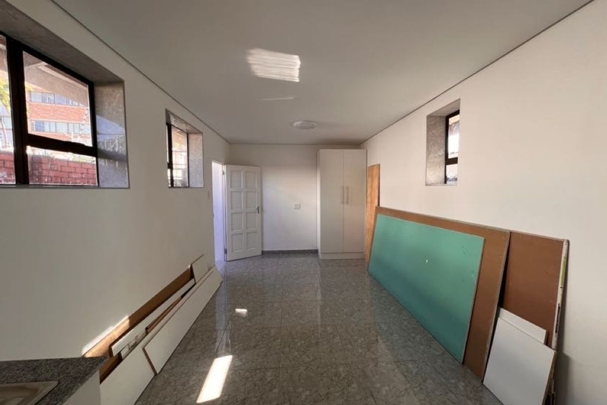 A spacious, empty bedroom featuring tiled flooring, built-in wardrobe, and natural light from multiple windows, currently undergoing minor finishing work.
