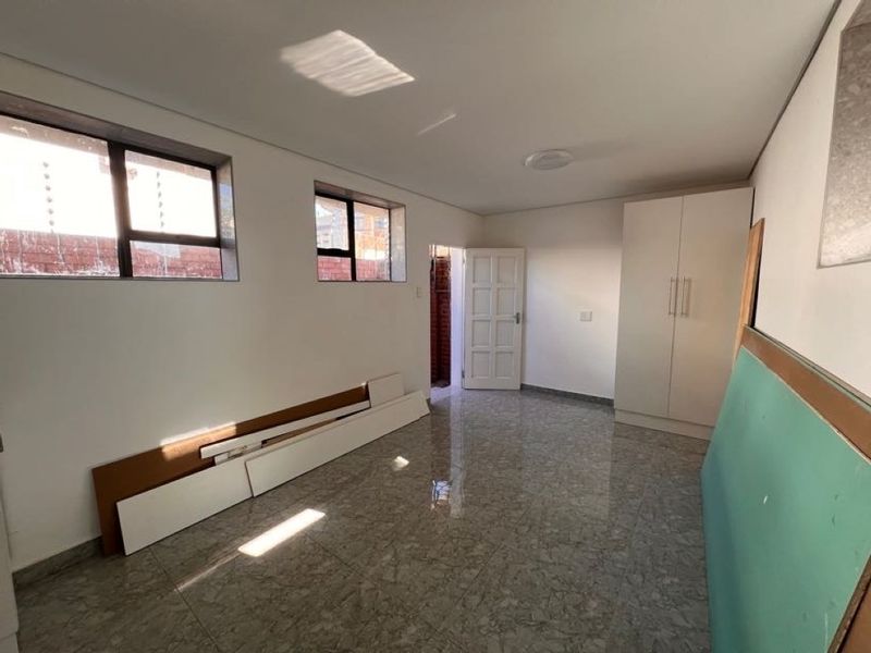 A bright, empty bedroom featuring tiled flooring, built-in wardrobes, and aluminium window frames, currently in a state of minor unfinished repair.