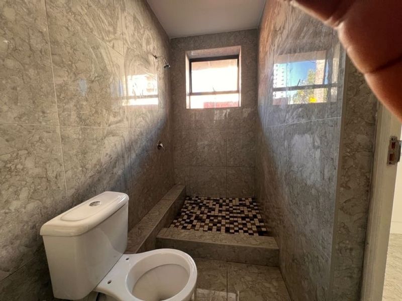 A compact bathroom featuring full-height marble-look wall tiling, a raised shower area with mosaic floor tiles, and a standard toilet.
