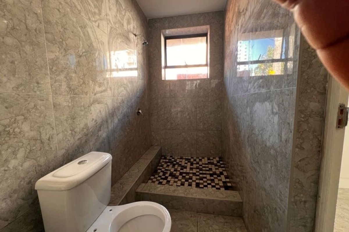 A compact bathroom featuring full-height marble-look wall tiling, a raised shower area with mosaic floor tiles, and a standard toilet.