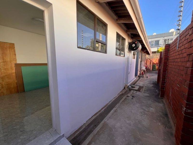 A side exterior view of the property featuring a concrete pathway, brick boundary wall, and aluminum window frames.