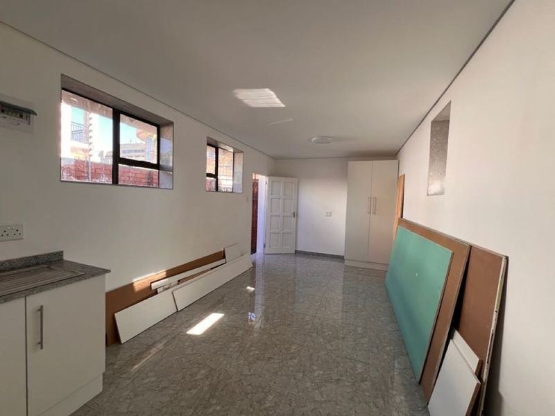 An open-plan living and kitchen area featuring tiled flooring, built-in cabinetry with granite countertops, and a built-in wardrobe, currently undergoing minor finishing work.