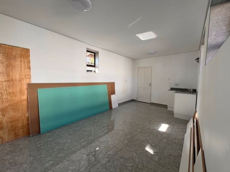 An empty, unfinished kitchen area featuring tiled flooring, basic cabinetry, and a sink, currently undergoing renovation or final completion.