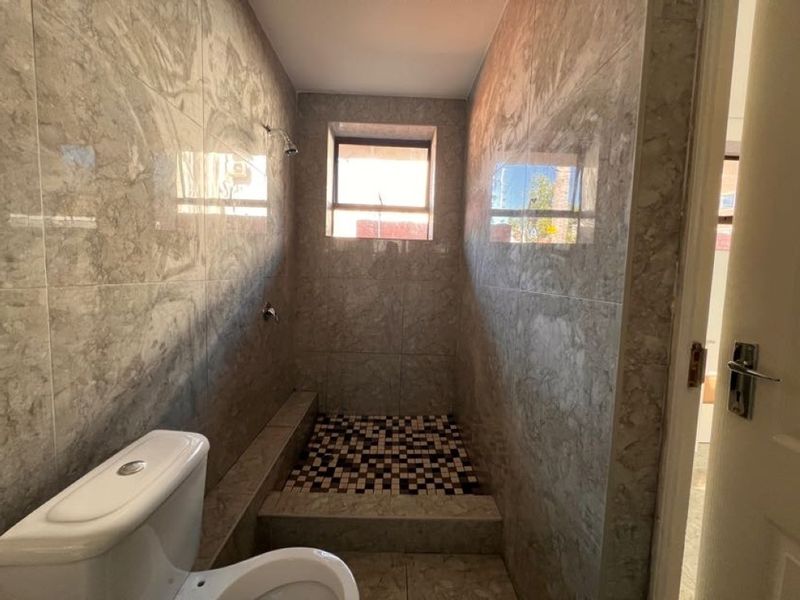 A modern bathroom featuring full-height marble-look wall tiles, a walk-in shower area with mosaic floor tiling, and a standard toilet.