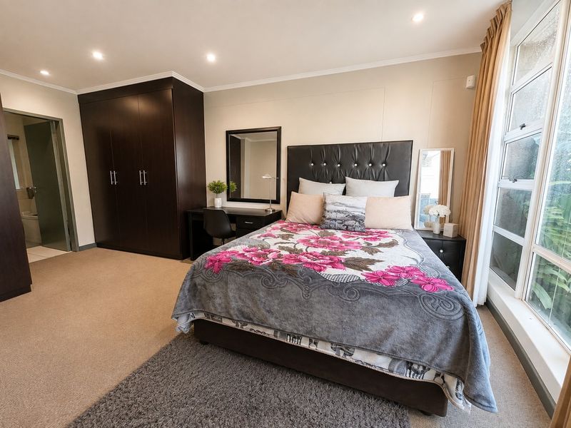 Spacious bedroom featuring neutral walls, carpet flooring, recessed downlighting, and a large window providing natural light, with an integrated dark wood wardrobe.