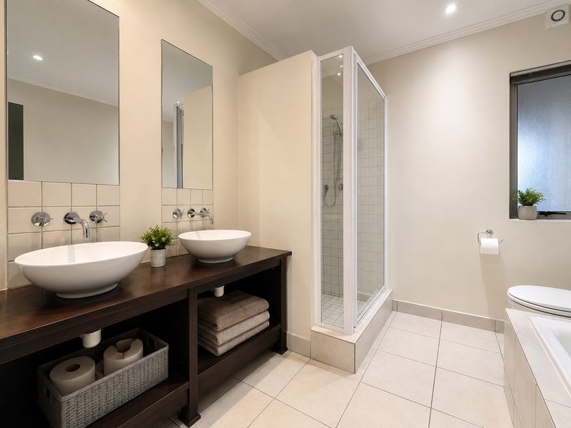 Modern bathroom featuring a double vanity with vessel sinks, wall-mounted faucets, a separate shower enclosure, and a built-in bathtub with tiled flooring.