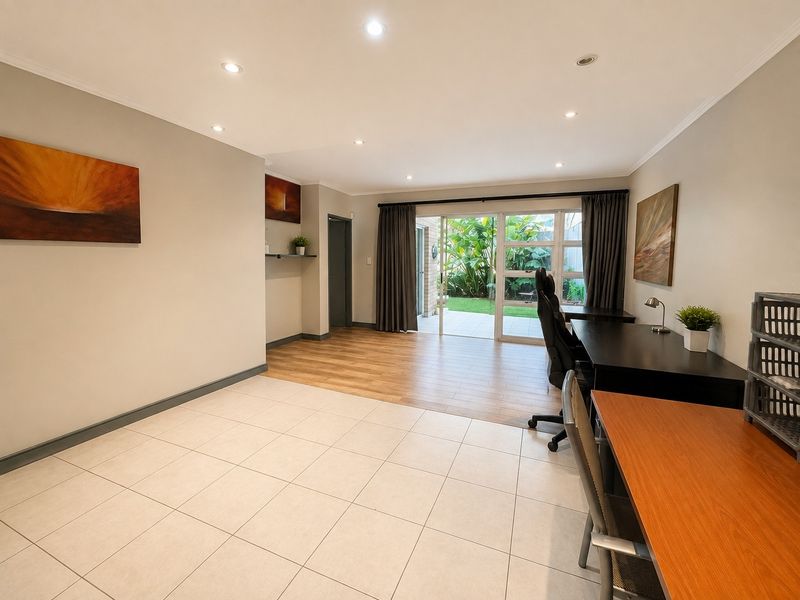 Spacious living area featuring a mix of ceramic tile and laminate wood flooring, with large sliding glass doors providing access to the garden.