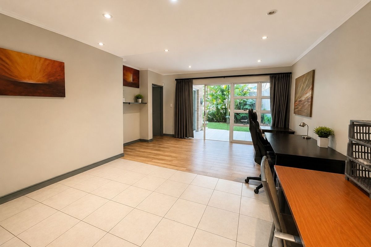 Spacious living area featuring a mix of ceramic tile and laminate wood flooring, with large sliding glass doors providing access to the garden.