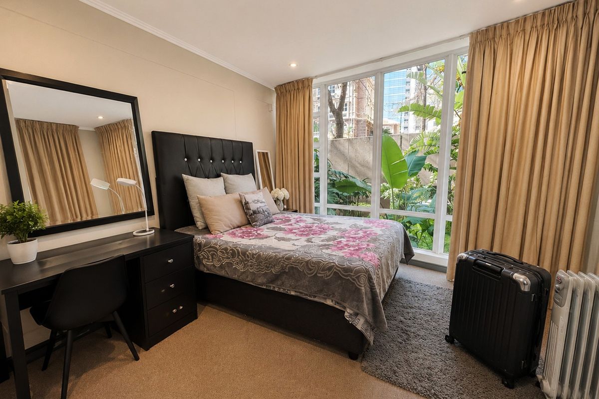 A well-lit bedroom featuring large floor-to-ceiling windows that provide natural light and a view of the surrounding greenery.