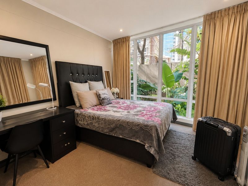 A well-lit bedroom featuring large floor-to-ceiling windows that provide natural light and a view of the surrounding greenery.