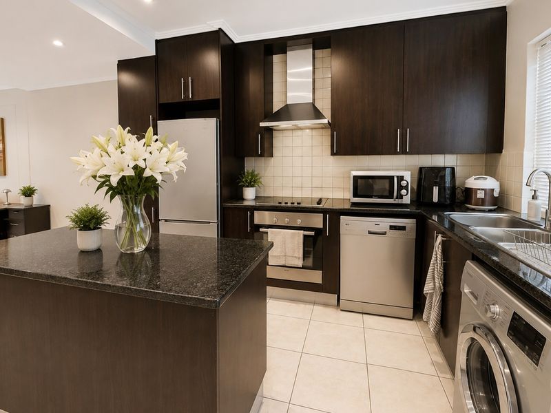 Modern kitchen featuring dark wood cabinetry, granite countertops, stainless steel appliances, and a functional kitchen island with tiled flooring.