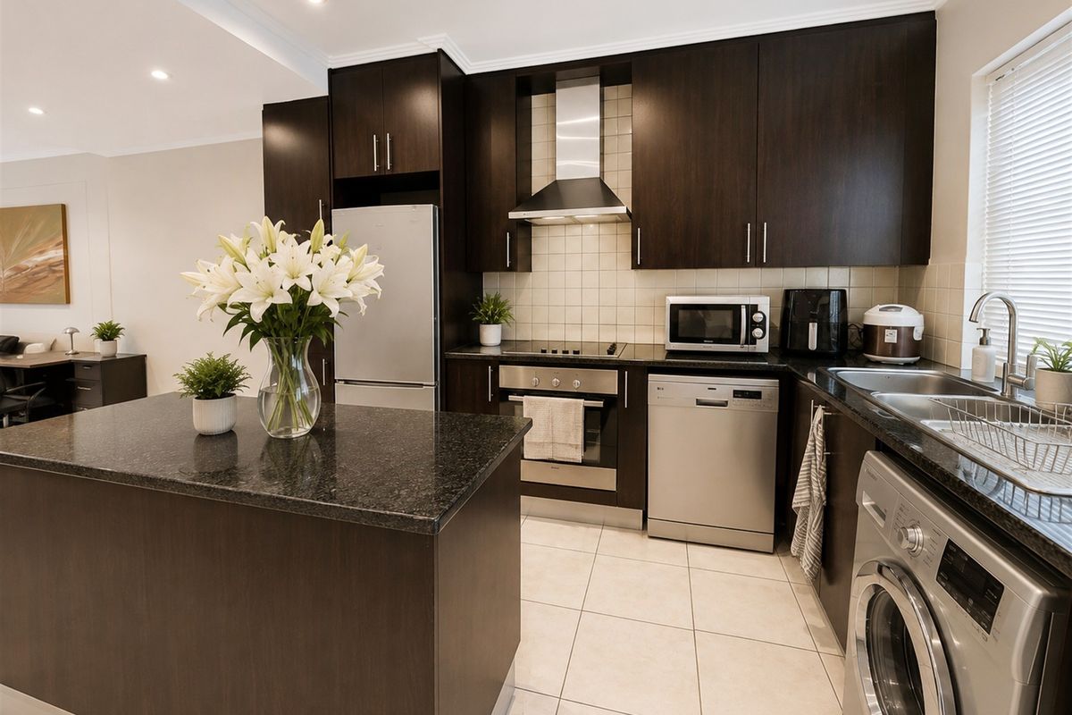 Modern kitchen featuring dark wood cabinetry, granite countertops, stainless steel appliances, and a functional kitchen island with tiled flooring.
