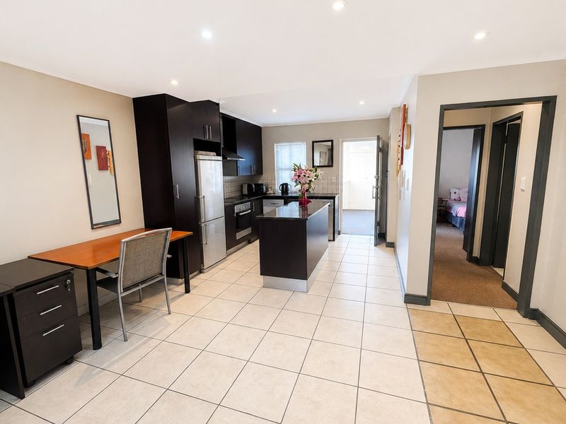 Open-plan kitchen and living area featuring dark wood cabinetry, granite countertops, built-in appliances, and neutral tiled flooring throughout.