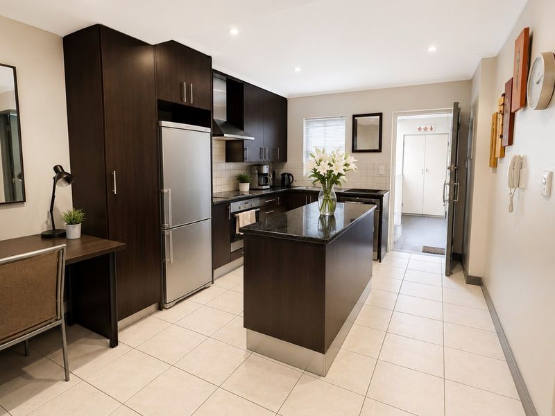 Modern kitchen featuring dark wood cabinetry, granite countertops, a central island, and tiled flooring, leading to a utility area.