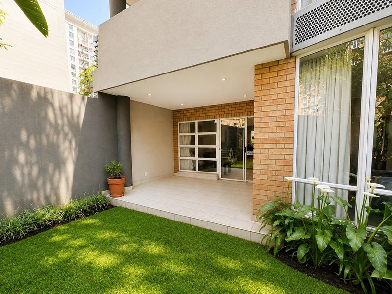 A well-maintained covered patio area featuring tiled flooring and recessed lighting, seamlessly connecting to a private garden space through sliding glass doors.