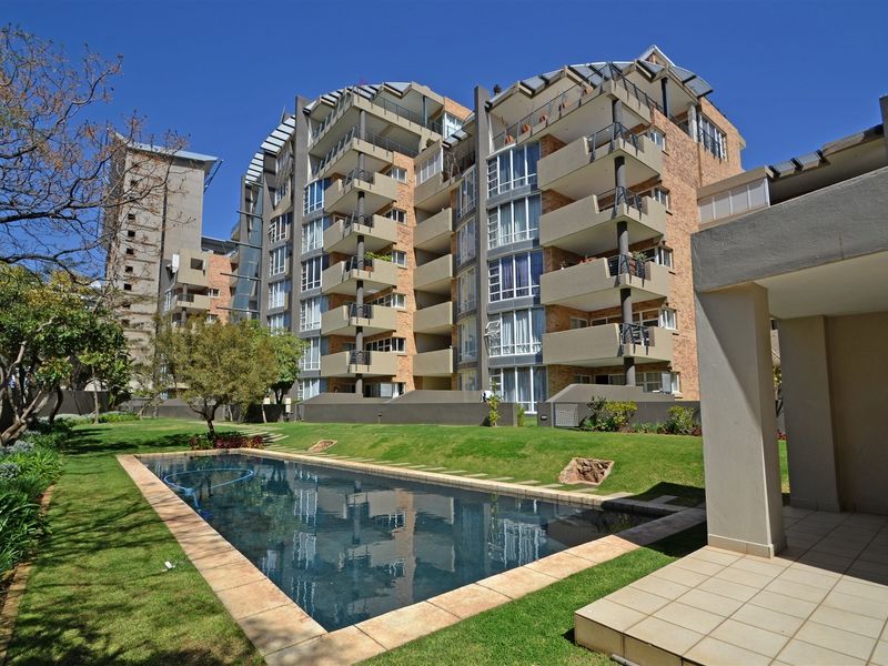 Exterior view of the apartment complex featuring a swimming pool, landscaped garden, and private balconies for the residential units.