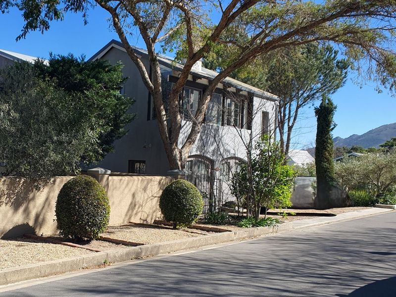 A view of the front elevation of the apartment building, featuring a boundary wall, wrought iron gate, and established garden landscaping.