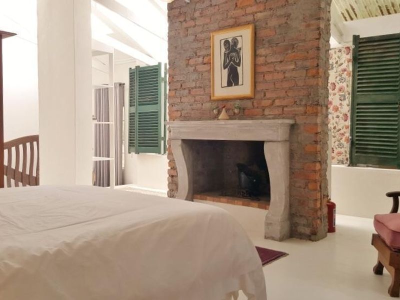 A characterful bedroom featuring an exposed brick fireplace with a stone mantelpiece, vaulted ceilings with exposed beams, and traditional louvre shutters.