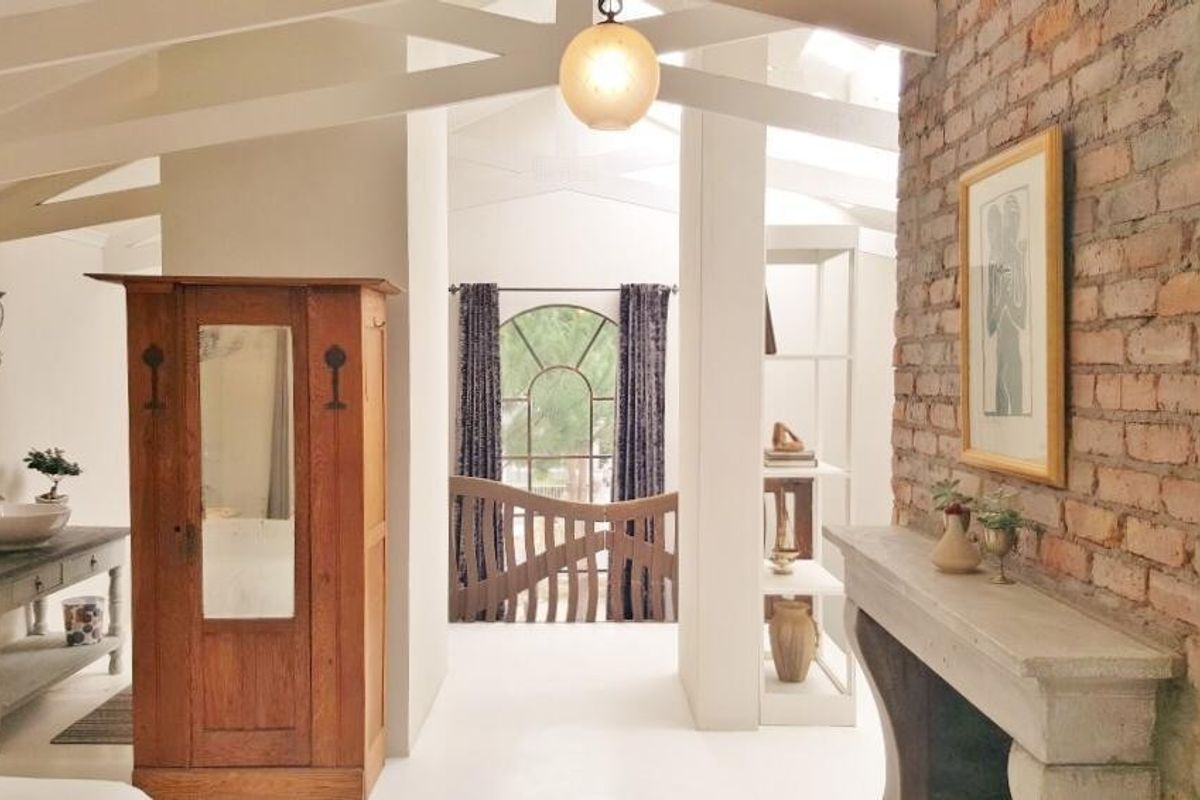 A characterful bedroom featuring an exposed brick wall, vaulted ceilings with exposed beams, and a stone fireplace mantel, creating a warm and rustic atmosphere.