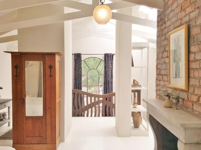A characterful bedroom featuring an exposed brick wall, vaulted ceilings with exposed beams, and a stone fireplace mantel, creating a warm and rustic atmosphere.