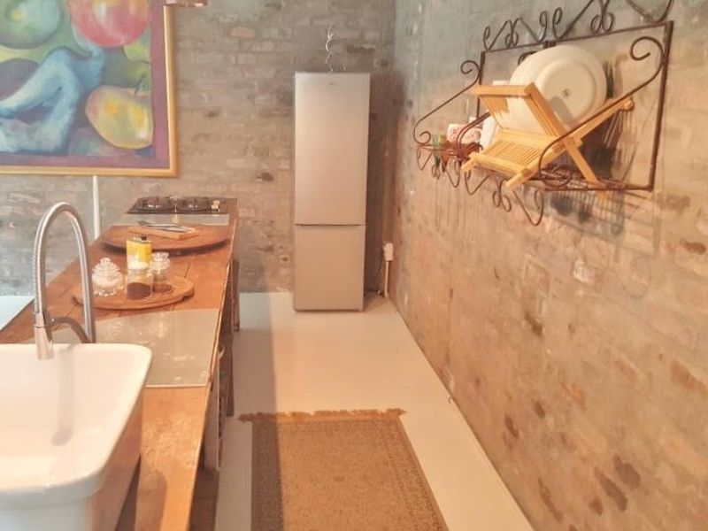 A rustic kitchen featuring exposed brick walls, a farmhouse-style apron sink with a gooseneck faucet, and a built-in cooktop.