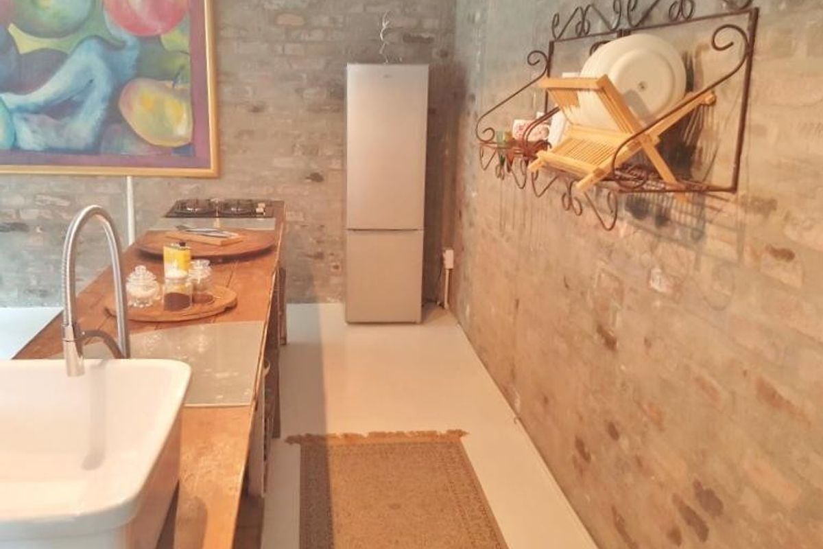 A rustic kitchen featuring exposed brick walls, a farmhouse-style apron sink with a gooseneck faucet, and a built-in cooktop.