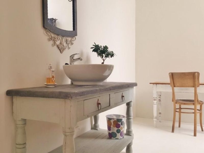 A bathroom vanity area featuring a vessel sink mounted on a painted wooden cabinet with a decorative wall mirror.