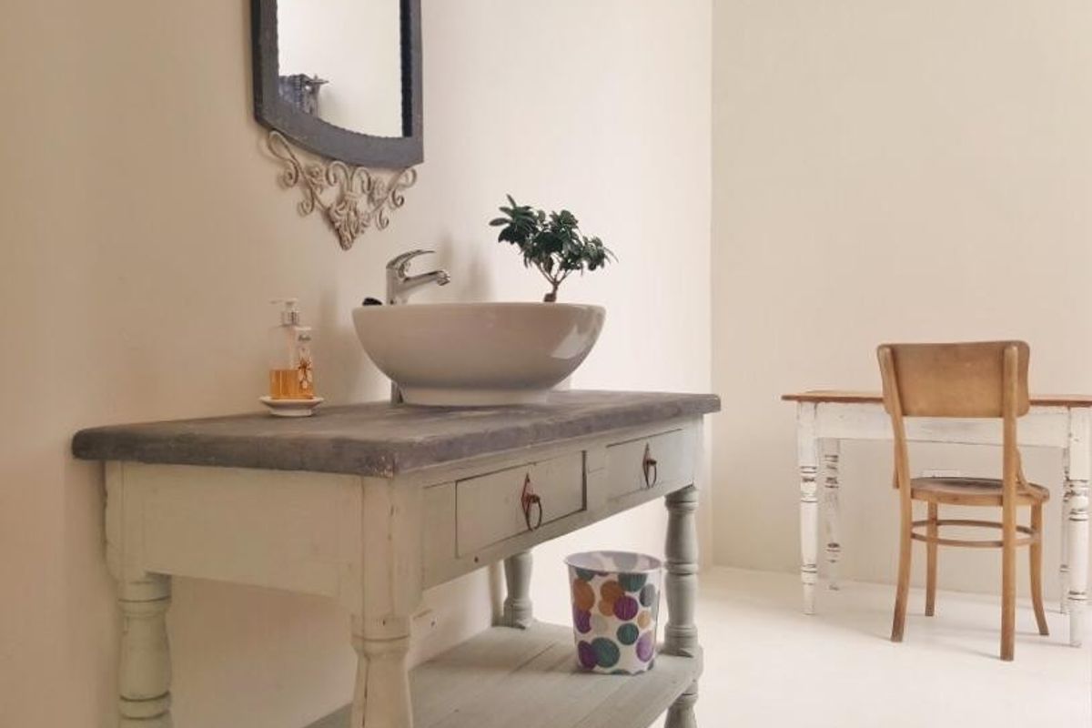 A bathroom vanity area featuring a vessel sink mounted on a painted wooden cabinet with a decorative wall mirror.