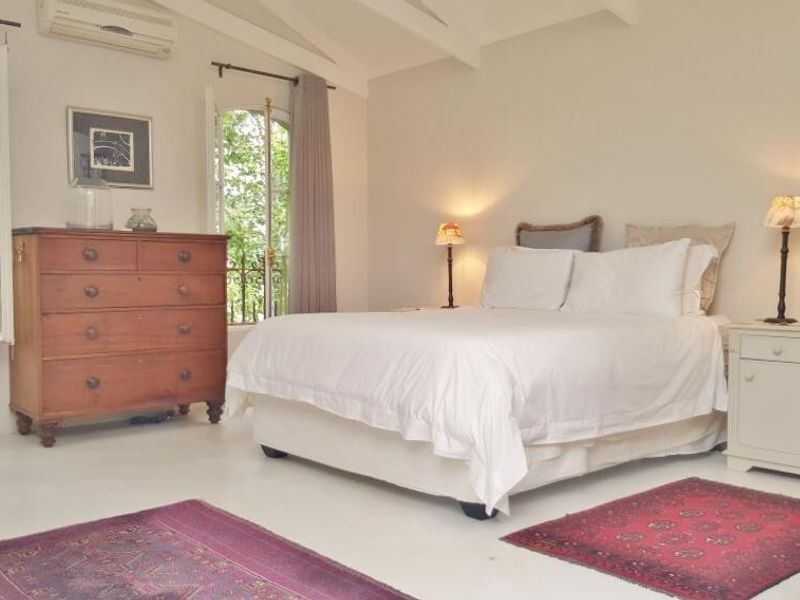 A bright bedroom featuring exposed ceiling beams, arched windows, and a wall-mounted air conditioning unit.