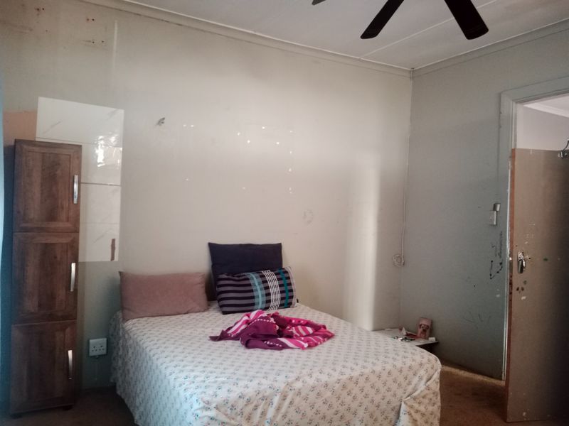 A bedroom featuring a ceiling fan and built-in cupboard storage, requiring cosmetic updates to the wall finishes and door frame.